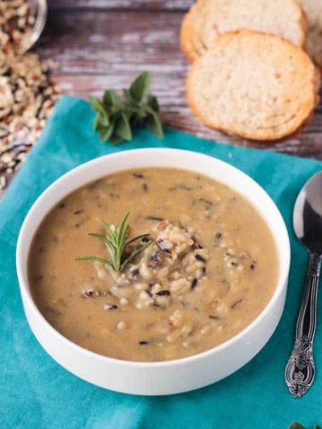 Bowl of wild rice soup on a blue kitchen towel. Slices of baguette in the background.