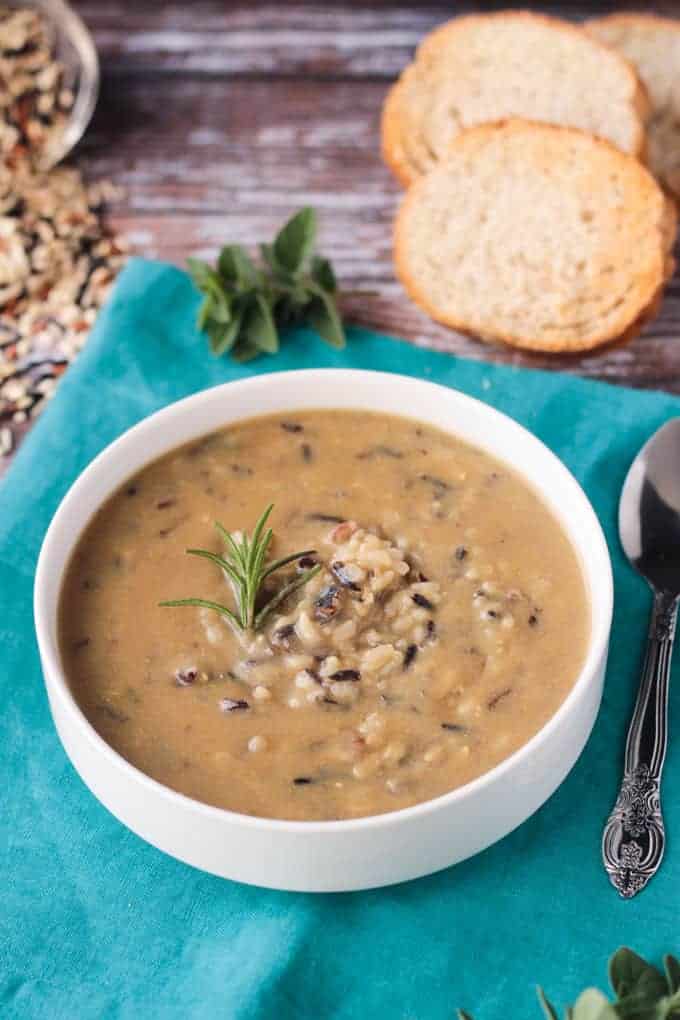 Bowl of wild rice soup on a blue kitchen towel. Slices of baguette in the background.