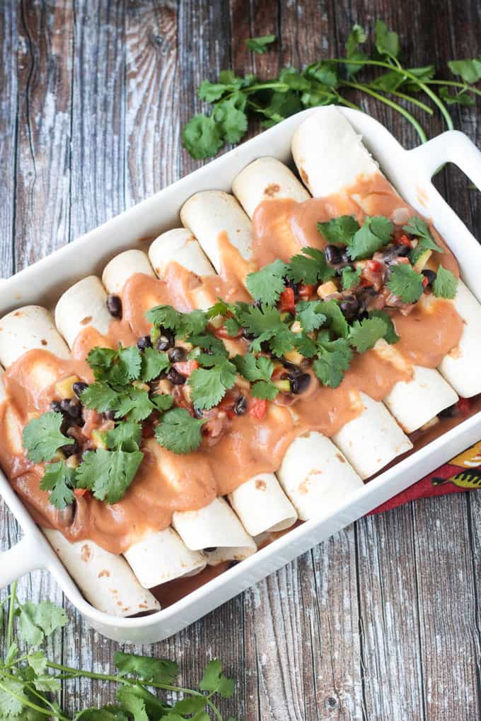 Black Bean & Zucchini Vegan Enchiladas - quick and easy and full of whole food ingredients like peppers, onion, zucchini, and beans. The sauce is made from white beans and salsa and comes together in just seconds. Top them off with lots of beautiful cilantro. These vegetarian enchiladas will quickly become a family favorite. Pan of enchiladas topped with salsa and lots of cilantro.