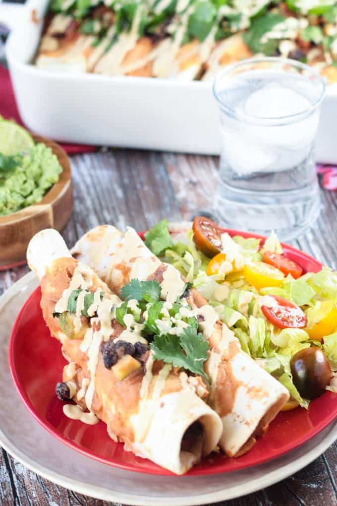 Two enchiladas on a red plate with salad. 