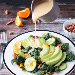 Orange Tahini Dressing being poured onto a lacinato kale salad.