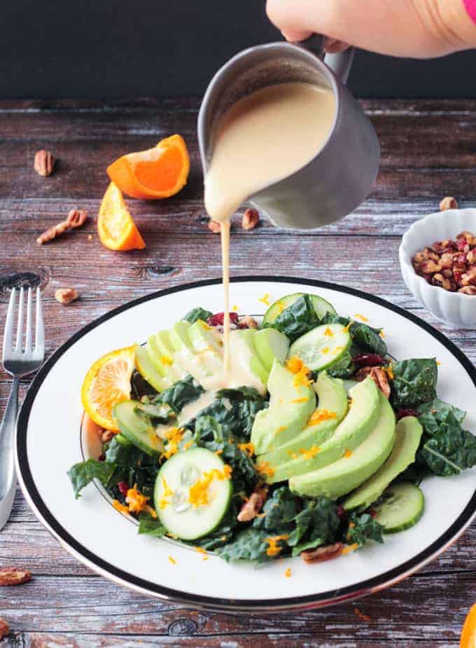 Orange Tahini Dressing being poured onto a lacinato kale salad.