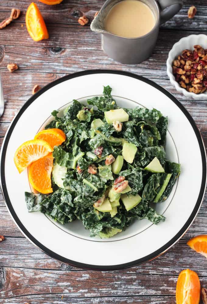 Bowl of kale salad with a small white bowl of pecans on the side.