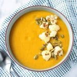 Bowl of sweet potato cauliflower soup on a blue/white dotted kitchen towel.