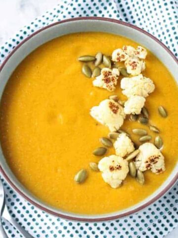 Bowl of sweet potato cauliflower soup on a blue/white dotted kitchen towel.