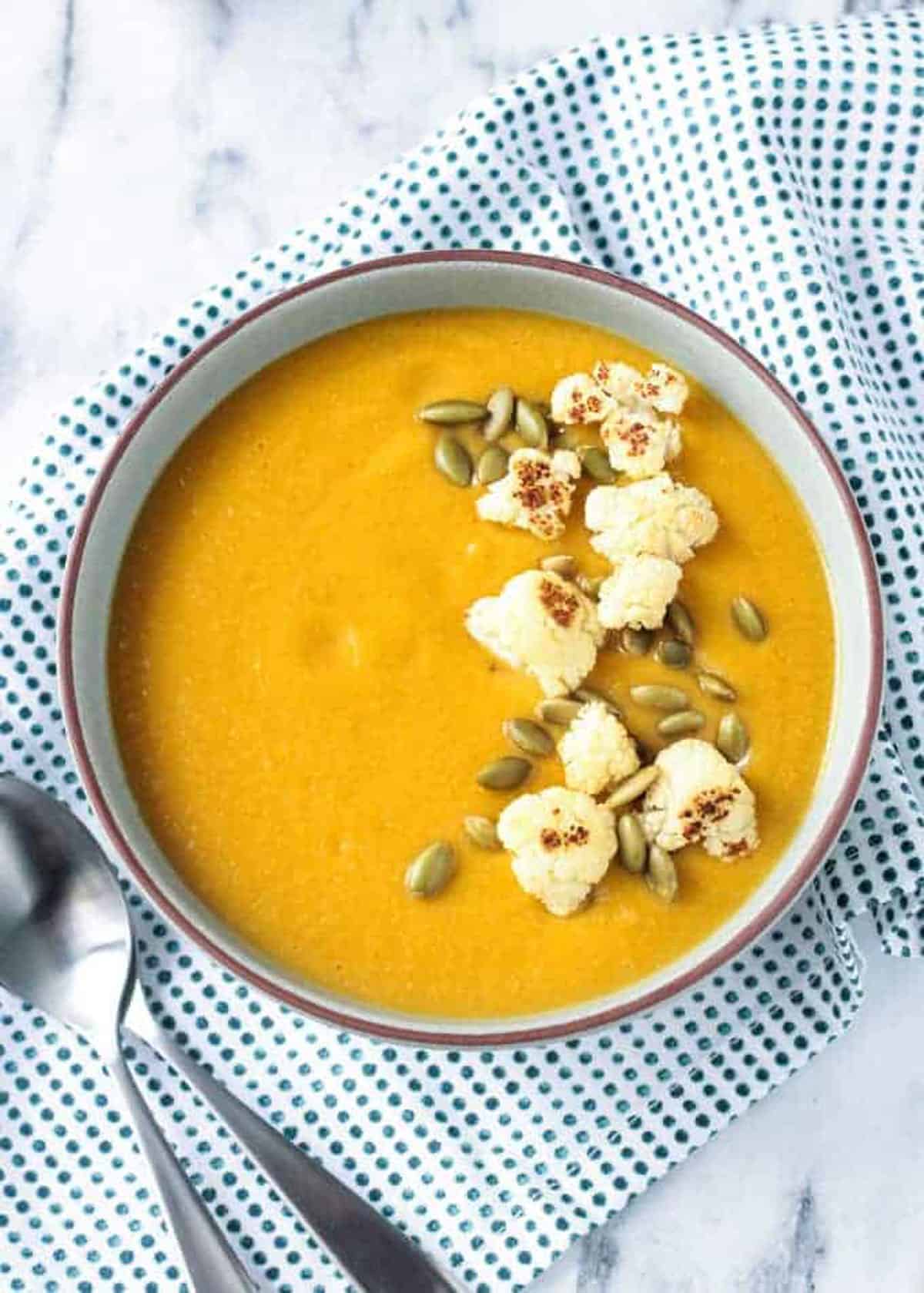 Bowl of sweet potato cauliflower soup on a blue/white dotted kitchen towel.