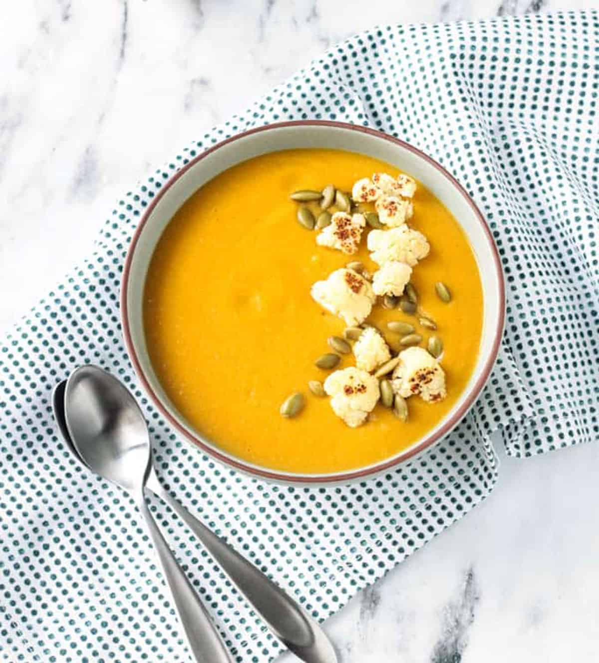 Bowl of sweet potato soup with two spoons lying nearby.