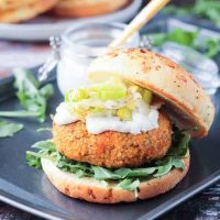 Autumn Vegan Burger with arugula, mayo, and caramelized leeks on an onion roll. The top half of the roll rests to the side of the burger.