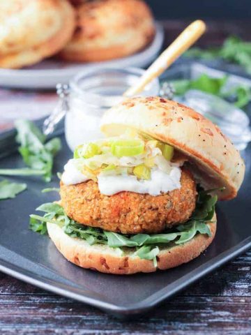 Autumn Vegan Burger with arugula, mayo, and caramelized leeks on an onion roll. The top half of the roll rests to the side of the burger.