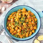 Bombay Potatoes and Peas in a blue skillet. Small dish or rice in the background.