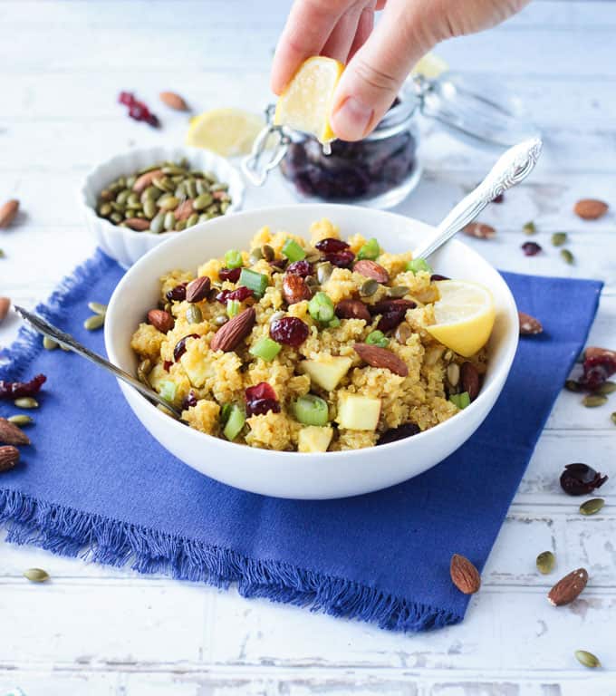 Hand squeezing a lemon over a bowl of curry quinoa salad.