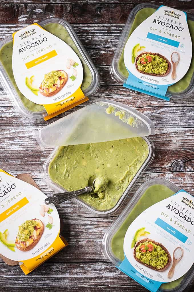 An open container of Simply Avocado guacamole dip surrounded by containers still in the package.