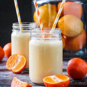 Two glasses of orange banana smoothie with orange and white striped straws.