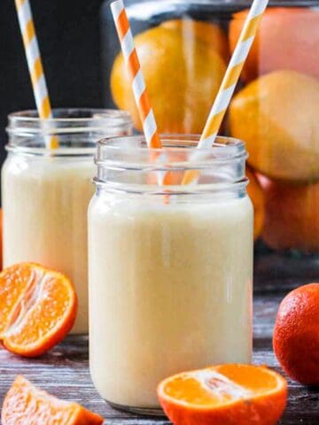 Two glasses of orange banana smoothie with orange and white striped straws.