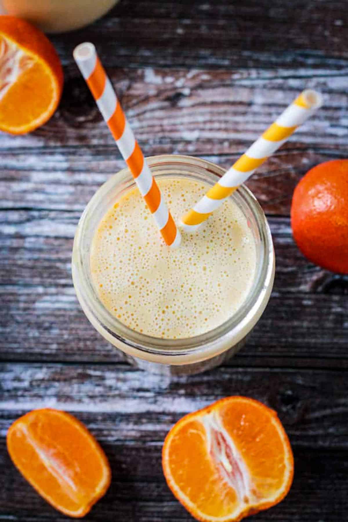 Overhead view of a creamy orange smoothie with two straws sticking out.