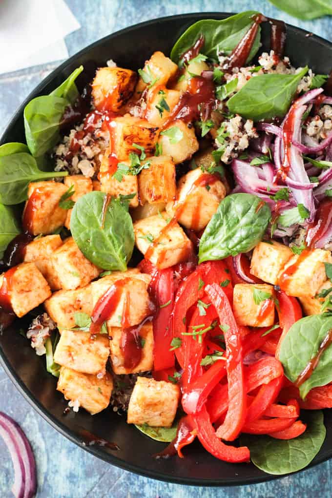 Overhead close up of baked tofu cubes and red pepper strips in a bowl drizzled with bbq sauce.