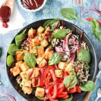 Overhead view of a BBQ Hawaiian Tofu Bowl w/ peppers, onions, pineapple, spinach, quinoa, and a drizzle of bbq sauce.