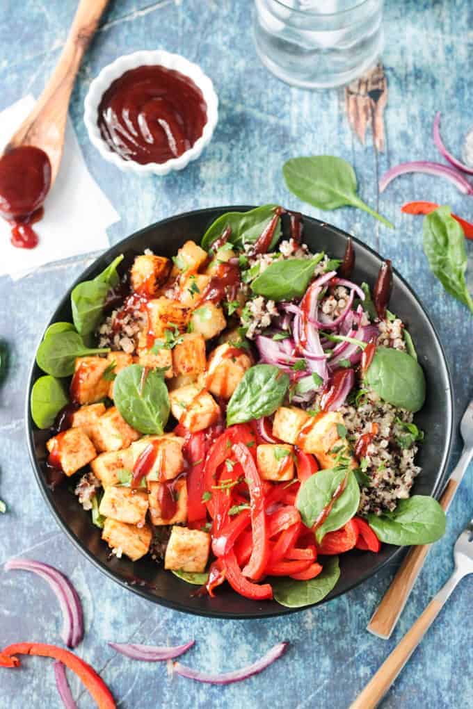 Overhead view of a BBQ Hawaiian Tofu Bowl w/ peppers, onions, pineapple, spinach, quinoa, and a drizzle of bbq sauce.