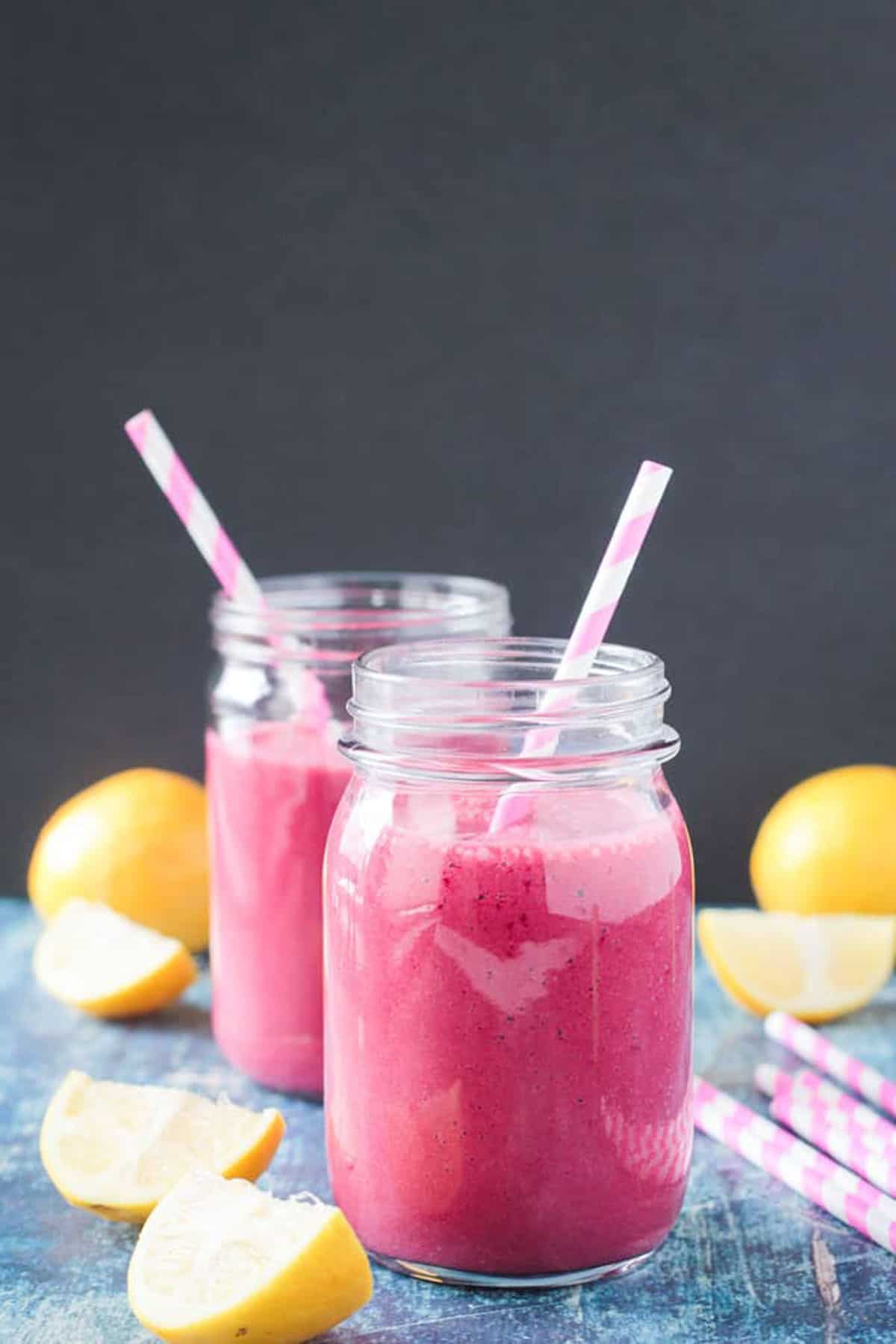 Two glass jars of hot pink smoothie with pale pink straws in each.