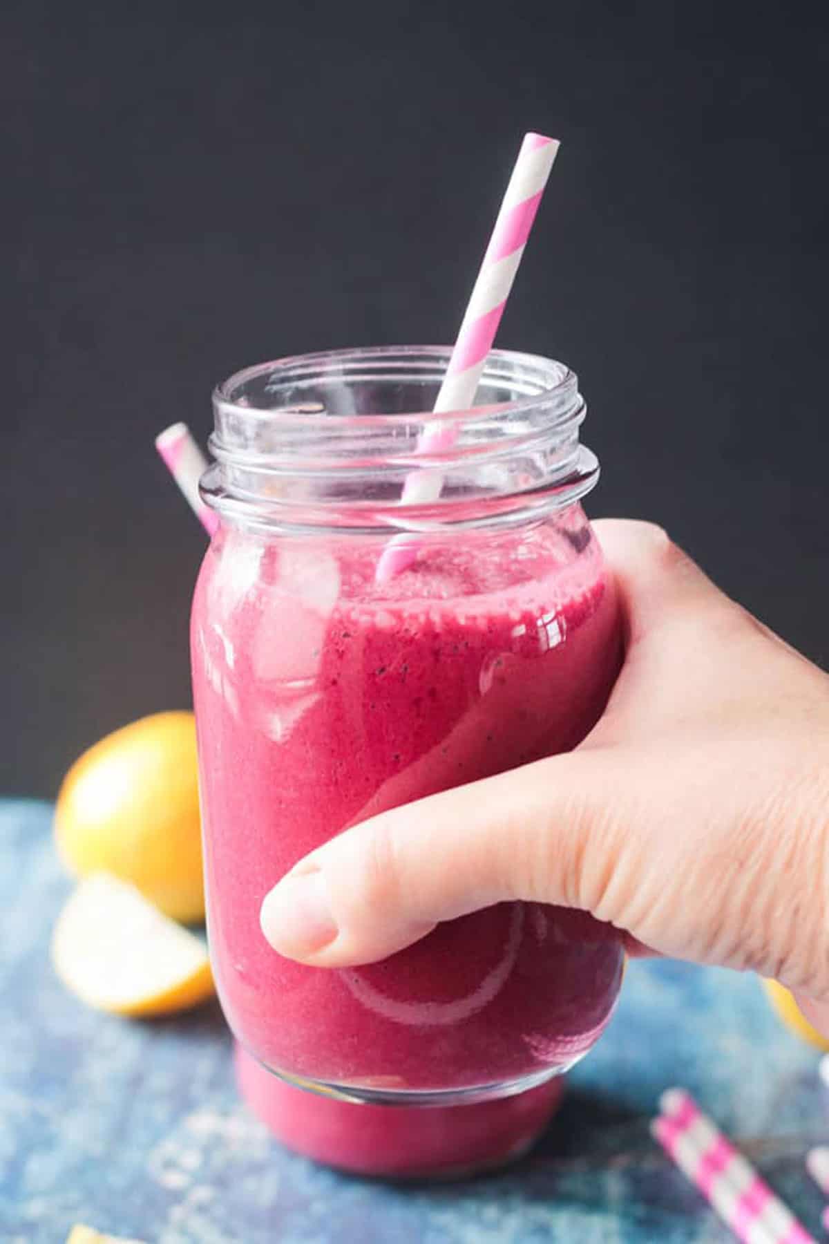 Hand holding up a pink strawberry beet smoothie.