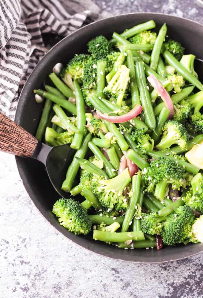 Close up overhead view of green bean broccoli stir fry in a skillet with a wooden handled serving spoon.