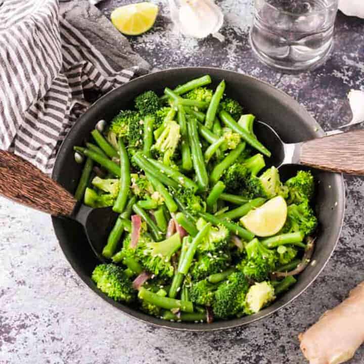 Broccoli, green beans, and red onion in a skillet with two serving spoons.