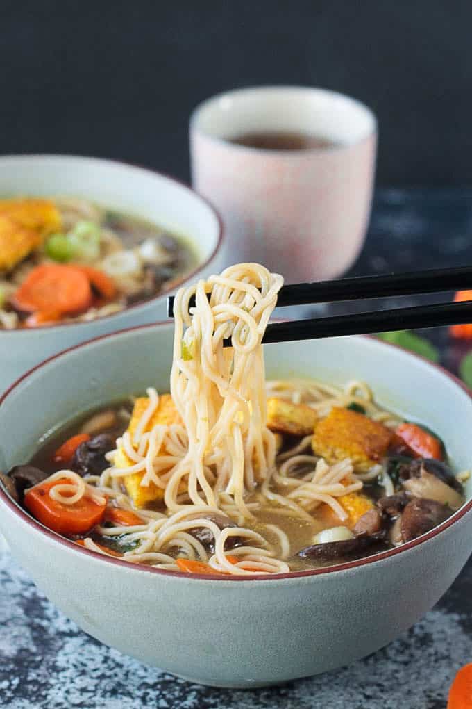 Chopsticks holding up a bite of noodles from a bowl.