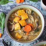 Overhead view of a bowl of mushroom ramen soup with carrots, spinach, and topped with crispy tofu.