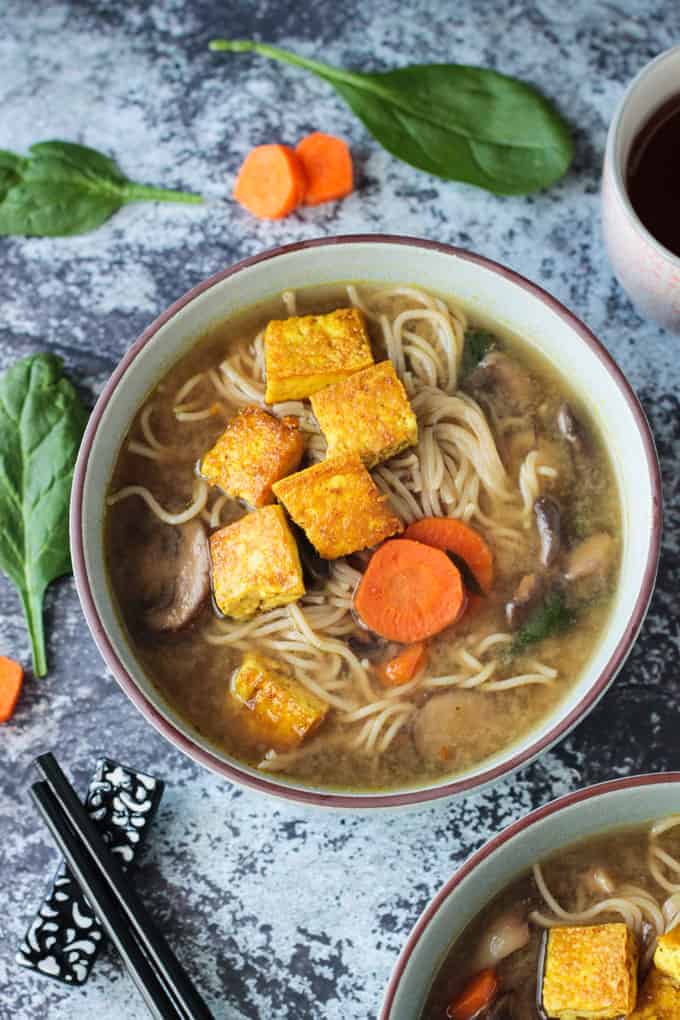 Overhead view of a bowl of mushroom soup with carrots, spinach, and topped with crispy tofu.