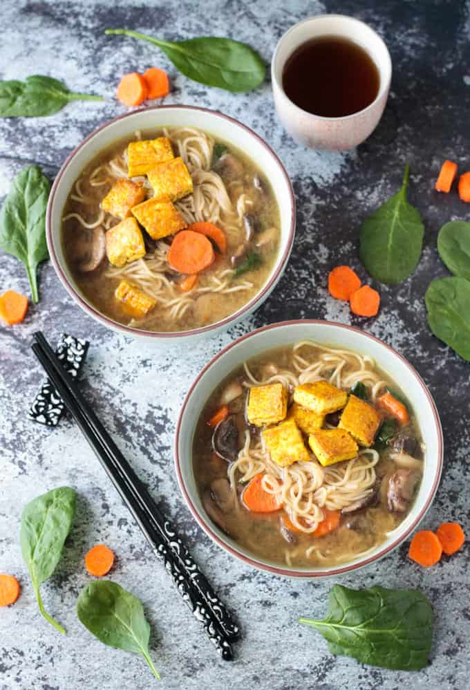 Two bowls of soup next to black chopsticks and fresh spinach leaves.