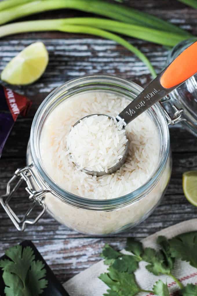 Small measuring cup in an open glass jar containing rice.