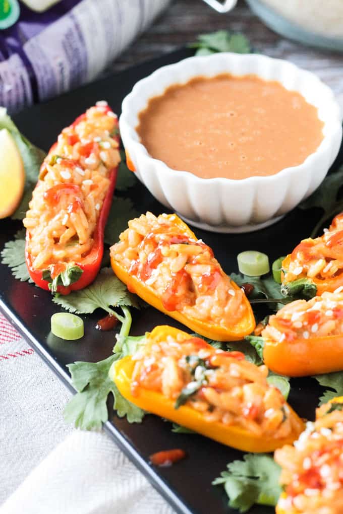 Spicy peanut rice stuffed mini peppers next to a bowl of spicy peanut sauce.