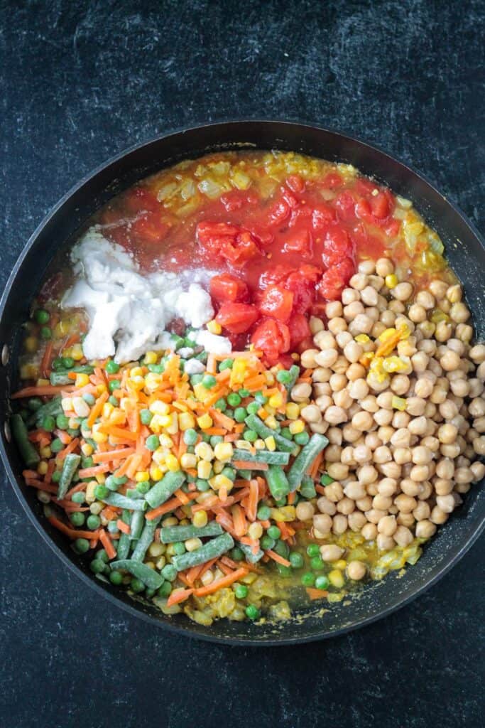 Diced tomatoes, frozen mixed vegetables, chickpeas, and coconut milk added to the skillet.
