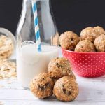 Three oatmeal peanut butter balls beside a glass of milk.