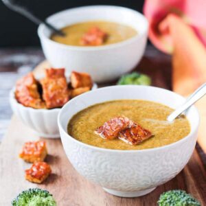 Two bowls of smoky vegan broccoli soup topped with crispy cubes of tempeh.
