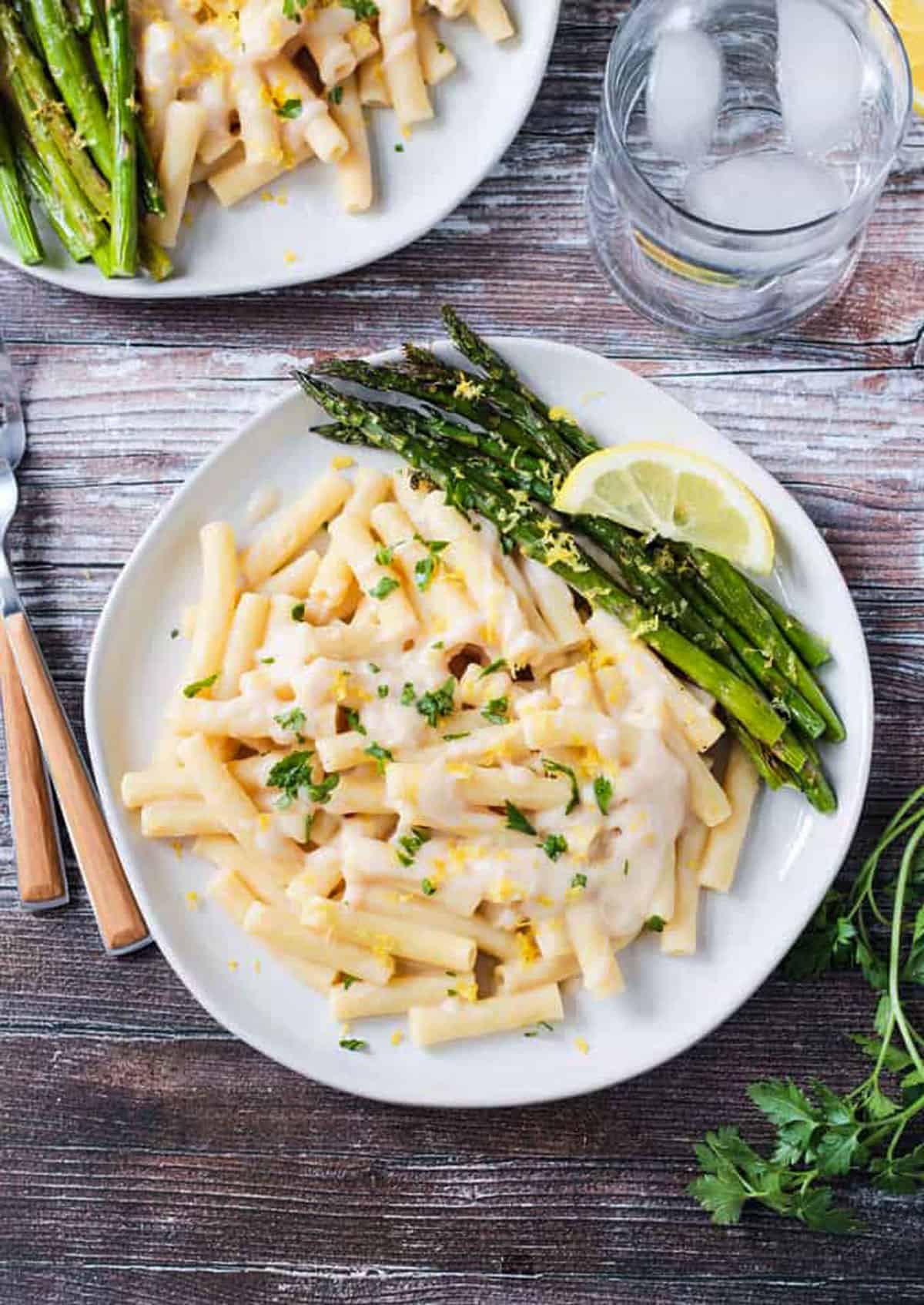 Overhead view of pasta in a vegan white sauce with a side of roasted asparagus.