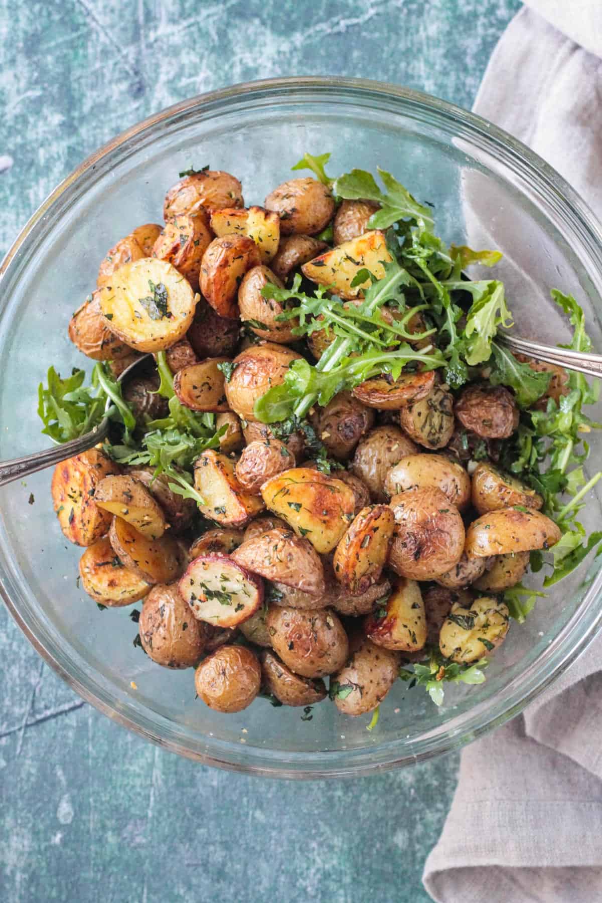 Hot roasted potatoes layered over arugula in a glass bowl.