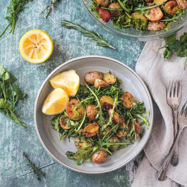 Arugula Salad with roasted potatoes plated next to two lemon wedges.