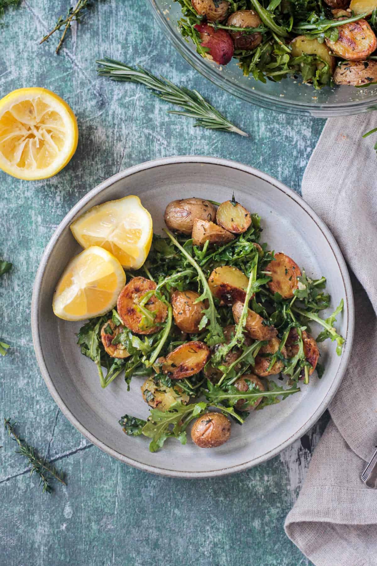 Arugula Salad with roasted potatoes plated next to two lemon wedges.