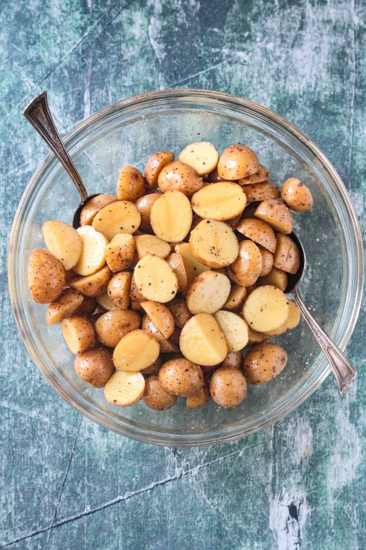 Halved baby potatoes in a glass bowl mixed with oil, salt, and pepper.