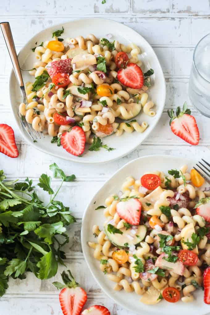 Two plates of summer pasta salad with a bunch of fresh parsley on the table in between.