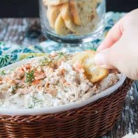 Hand dipping a baguette slice into a bowl of cold crab dip.