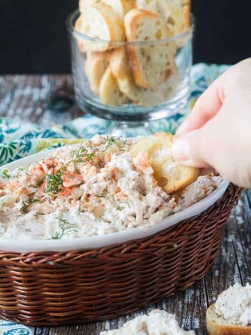 Hand dipping a baguette slice into a bowl of cold crab dip.