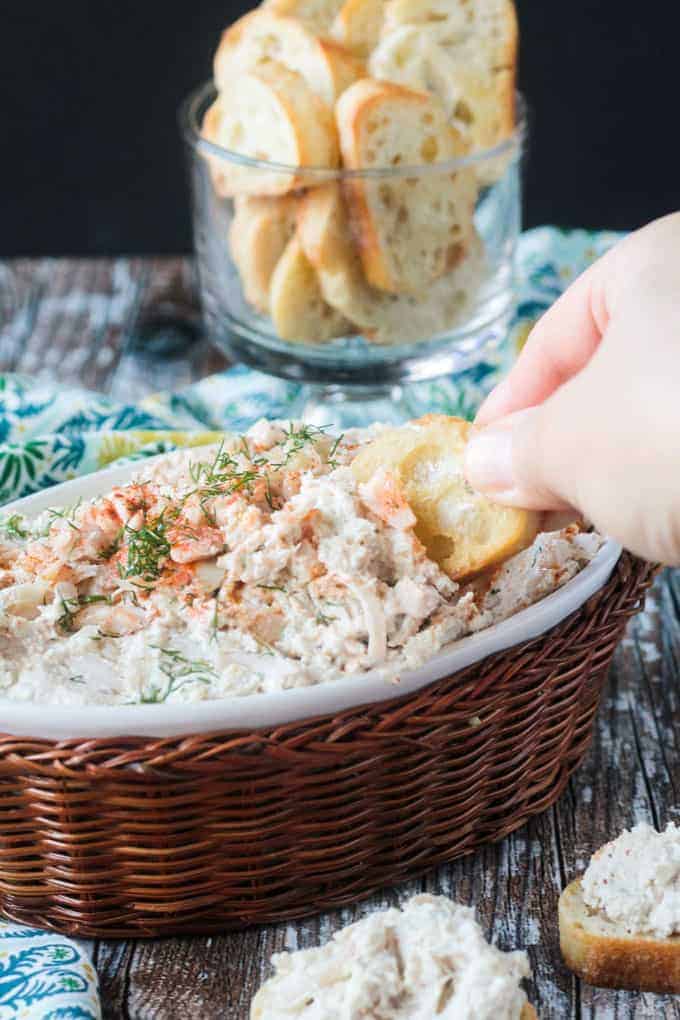 Hand dipping a baguette slice into a bowl of cold crab dip.