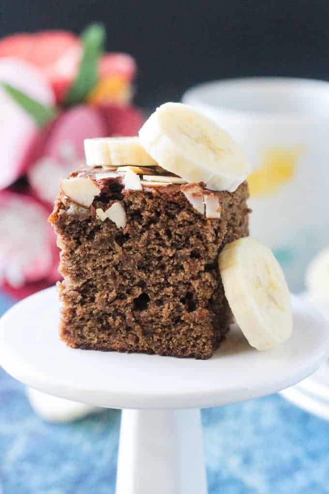 Square slice of banana bread cake toped with fresh banana slices and slivered almonds.