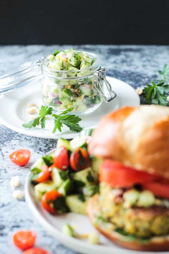 Jar of cucumber peanut relish in focus in the background. Falafel burger in the foreground off to the side and out of focus.