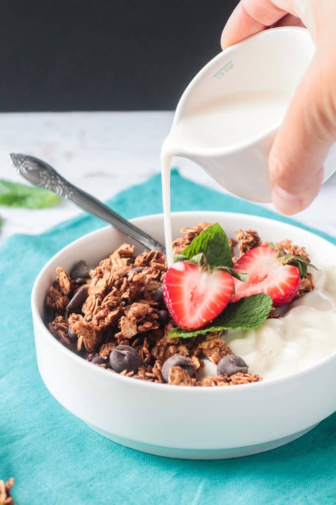 Milk being poured from a small white pitcher onto a bowl of granola.