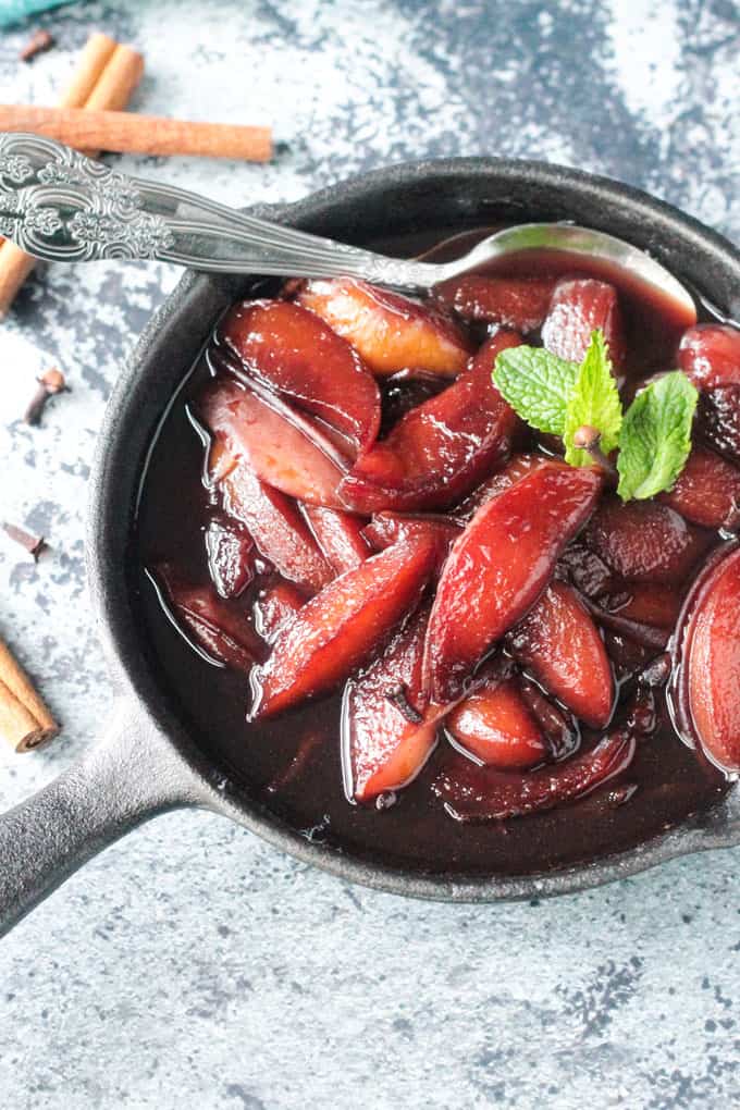 Two metal spoons in a cast iron skillet full of poached nectarines in red wine.