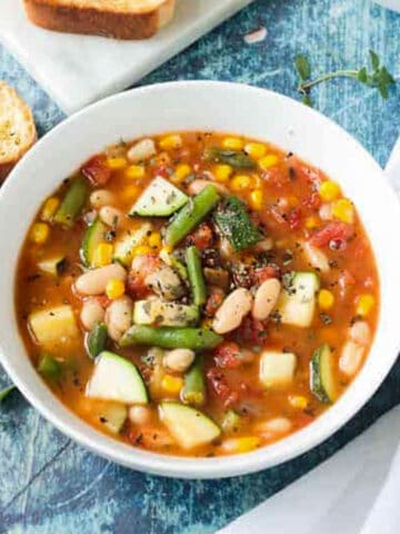 Loaf of sliced bread behind a bowl of summer white bean vegetable stew.