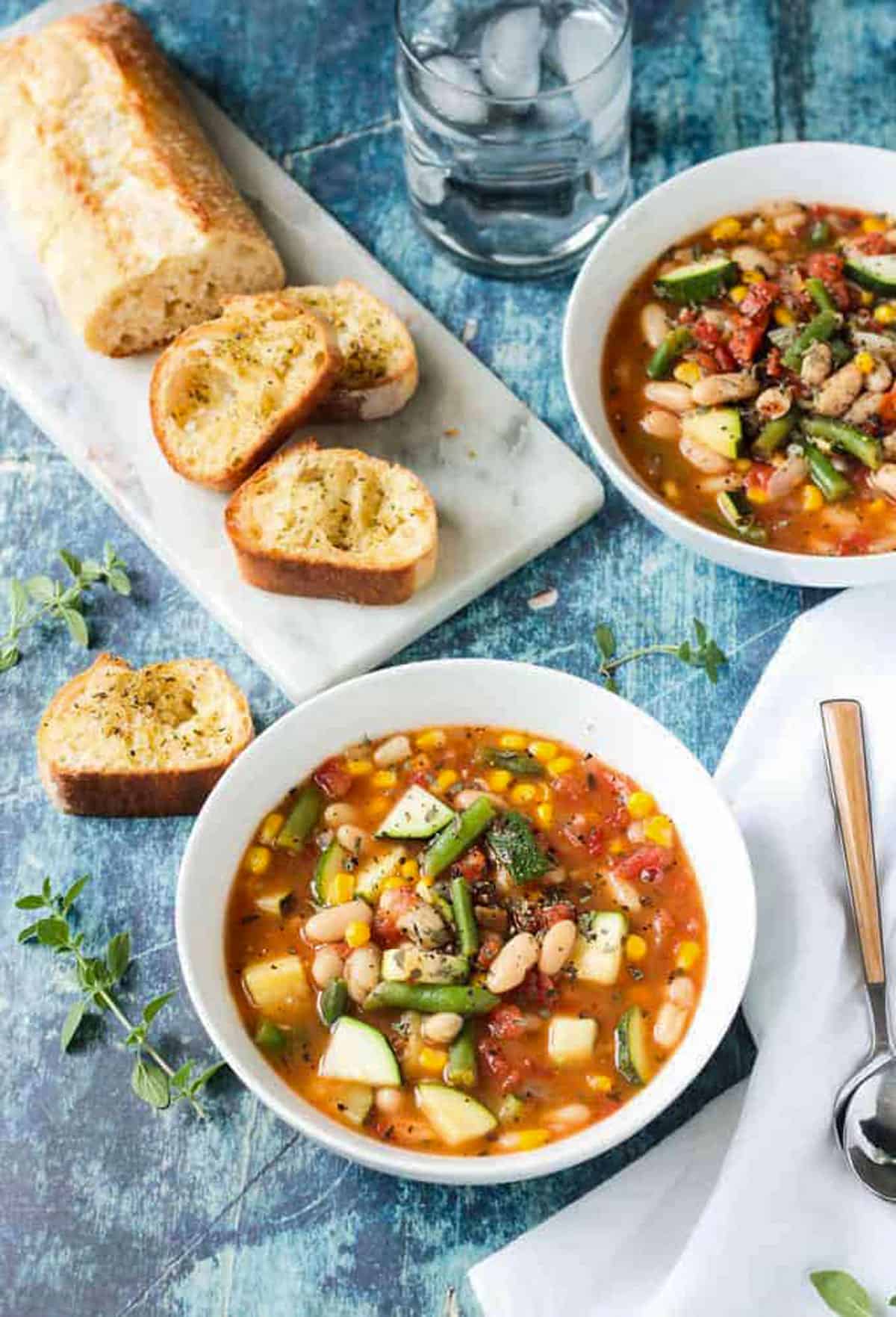 Summer Stew from Vegan Yack Attack On The Go - an easy vegetable and white bean soup recipe that uses the best of summer garden offerings. Perfect for a healthy lunch or pair it with a loaf of crusty bread for a hearty dinner. It all comes together in less than 30 minutes! Loaf of sliced bread behind a bowl of summer white bean vegetable stew.